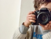 Ein Kind hält eine Kamera in den Händen. Der Umgang mit Fotos in der Kita sollte mit Eltern und im Team thematisiert werden.