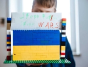 Kind mit ukrainischer Legofahne und einem Schild, auf dem "Stopp War" steht