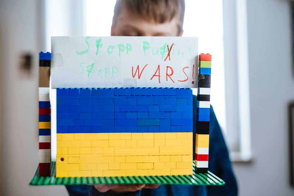 Kind mit ukrainischer Legofahne und einem Schild, auf dem "Stopp War" steht